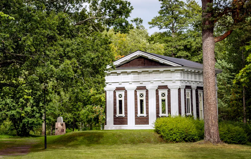 Ett litet brunvitt hus ligger vackert i en lummig park.