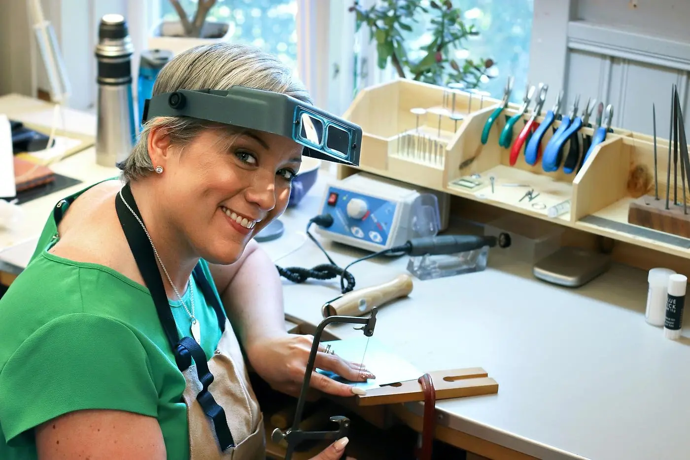 Silversmeden Veronica med uppdragna skyddsglasögon vid sin arbetsbänk med små tänger och andra verktyg. 