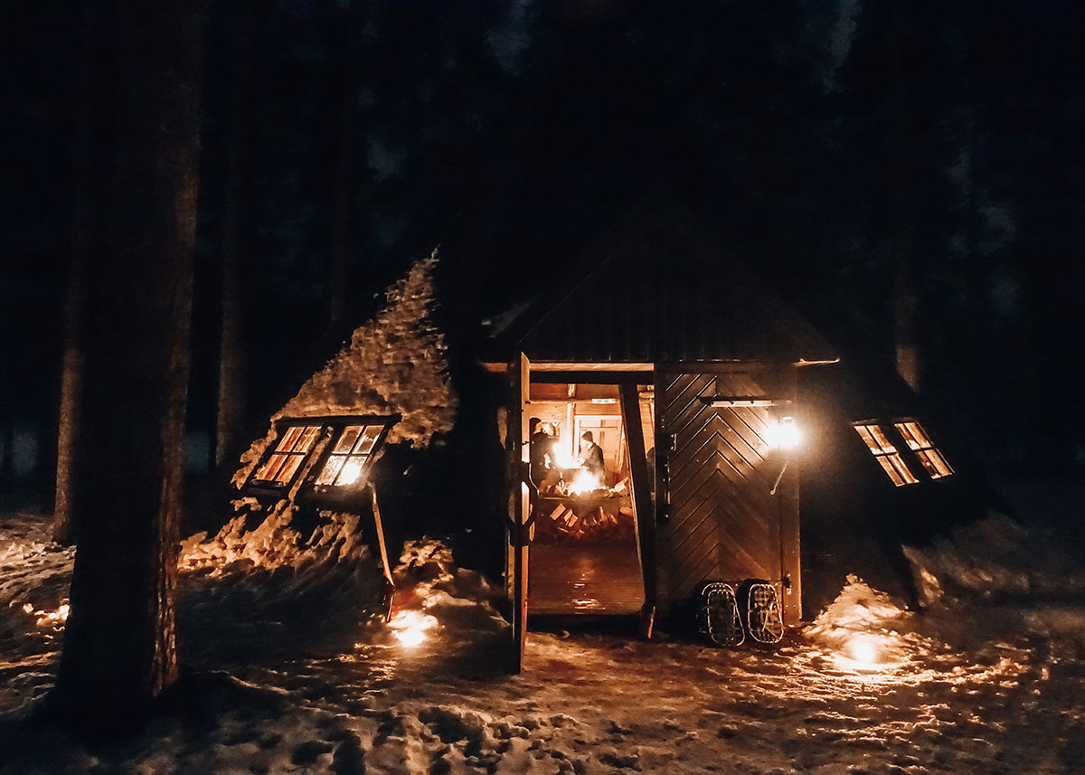Ett sällskap äter middag i en varm stuga i skogen en kväll vinterkväll.