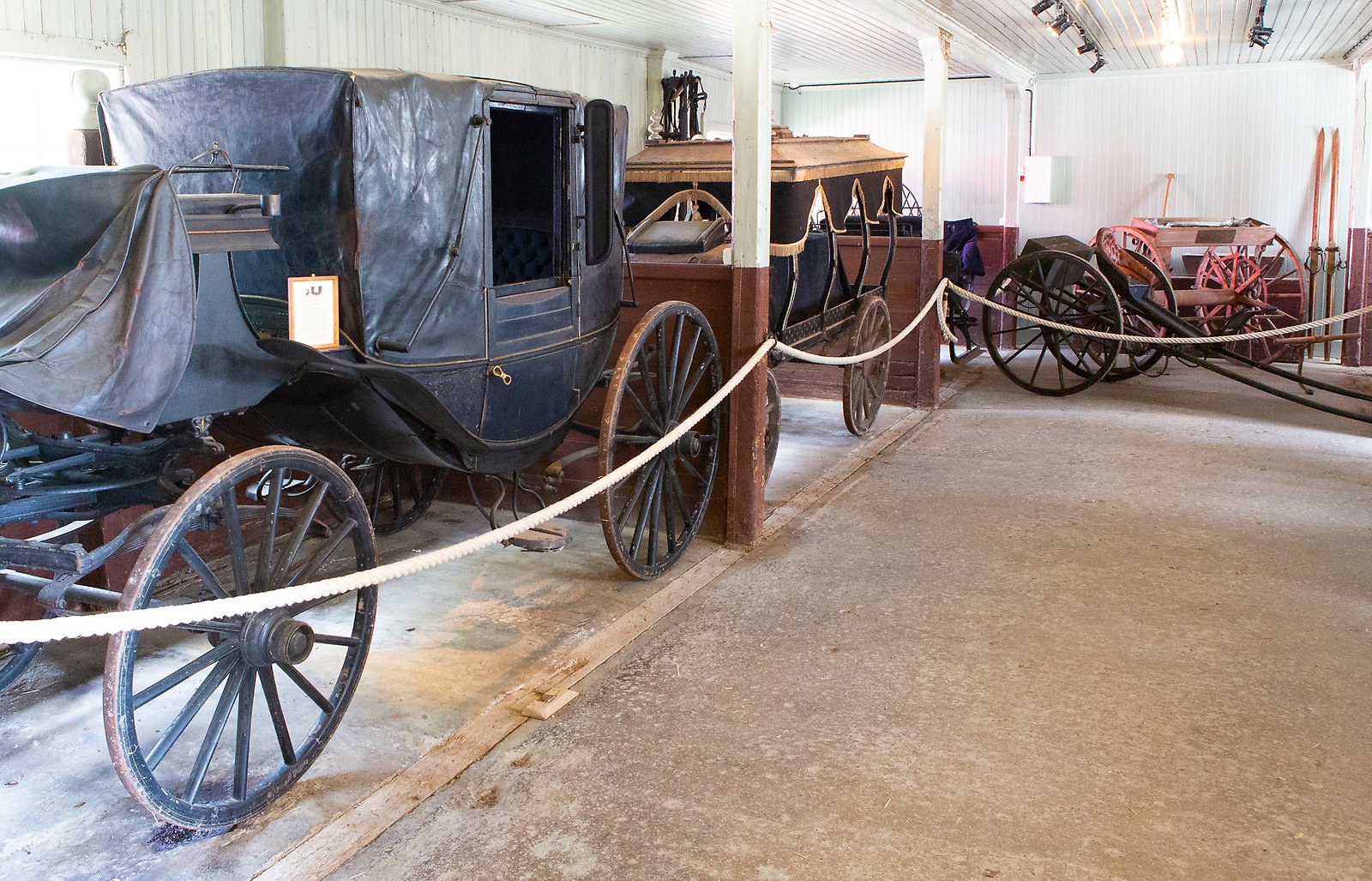 Antika vagnar står uppställda i ett vitmålat gammalt stall