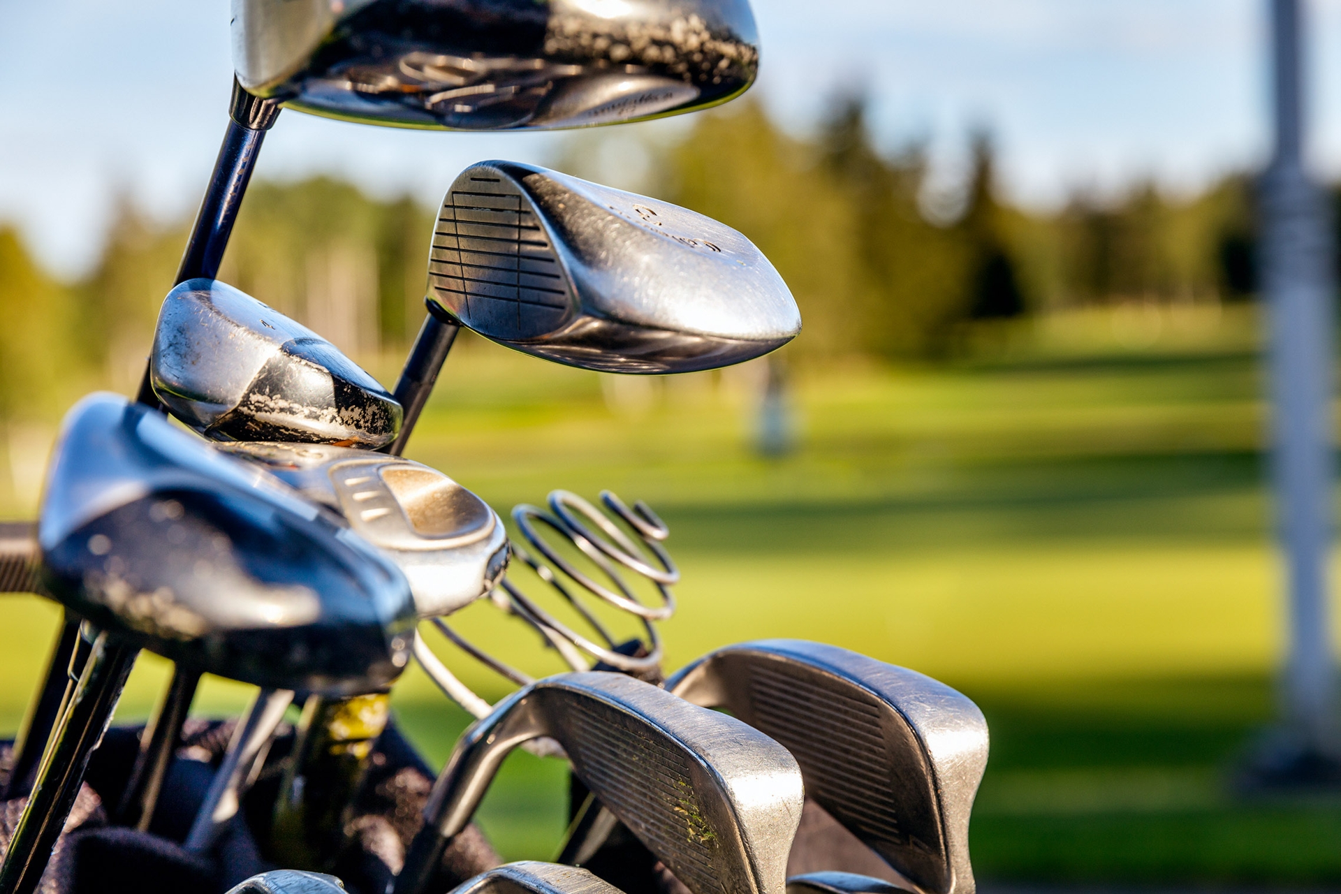 Närbild av golfklubbor med en grön golfbana i bakgrunden