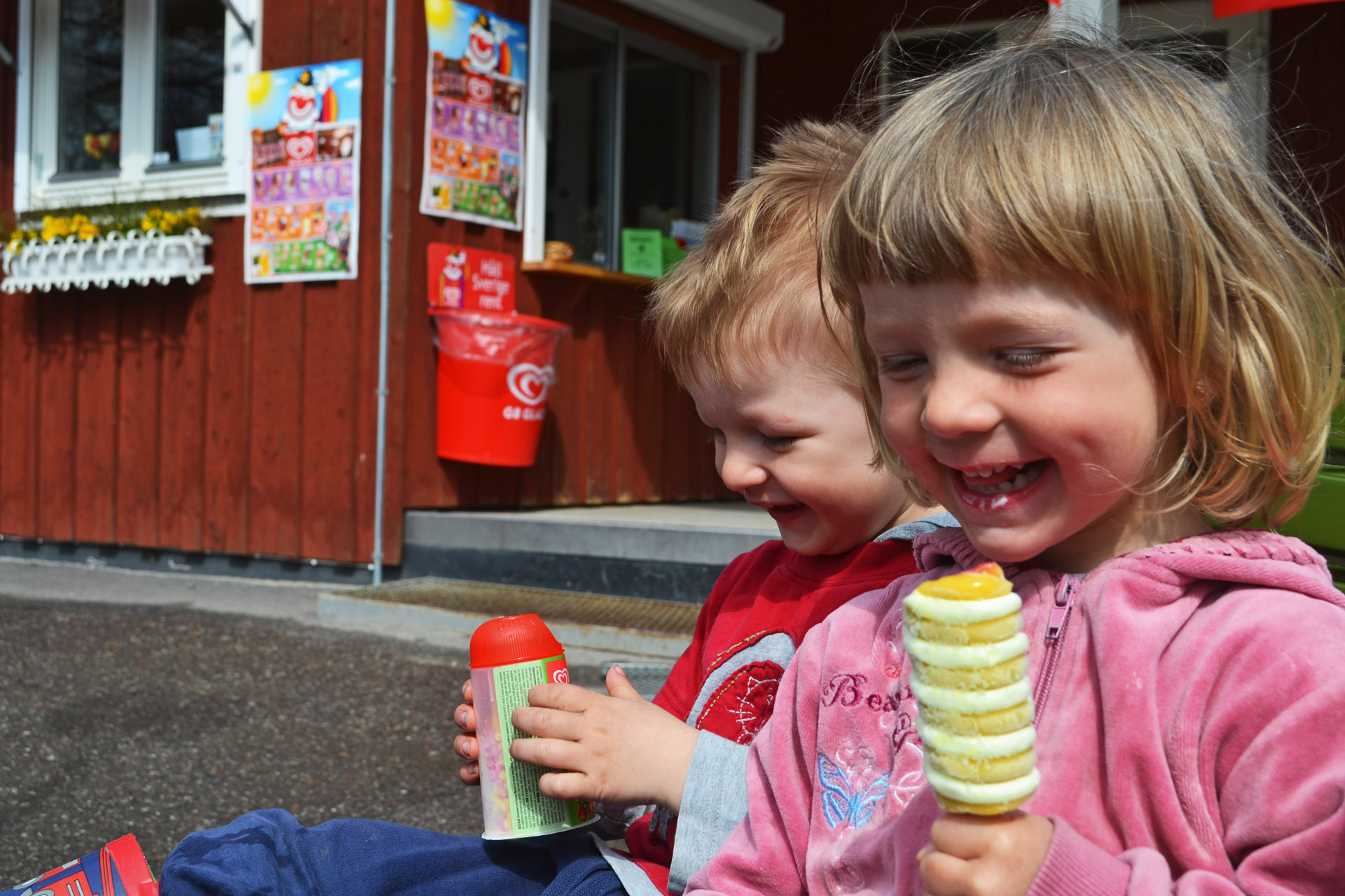 Två små barn äter glass i solskenet utanför kiosken