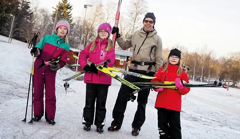 Tre barn och en vuxen som bär på längdskidor
