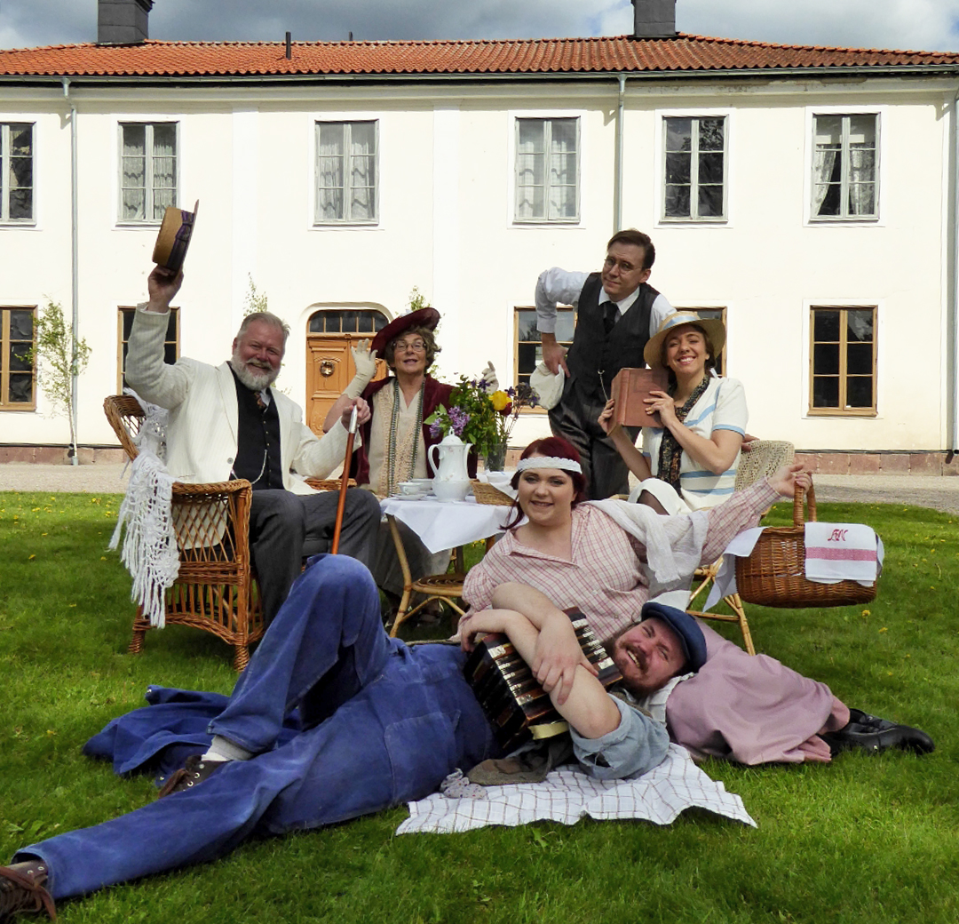 En teatergrupp i historiska kläder på gräsmattan framför Gamla Herrgården
