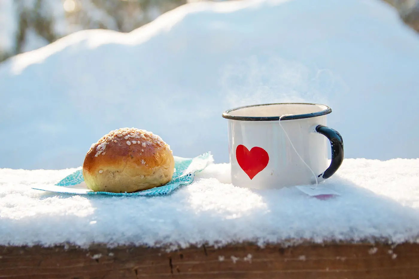 En bulle och en kopp rykande te, uppdukat på ett snöigt bord