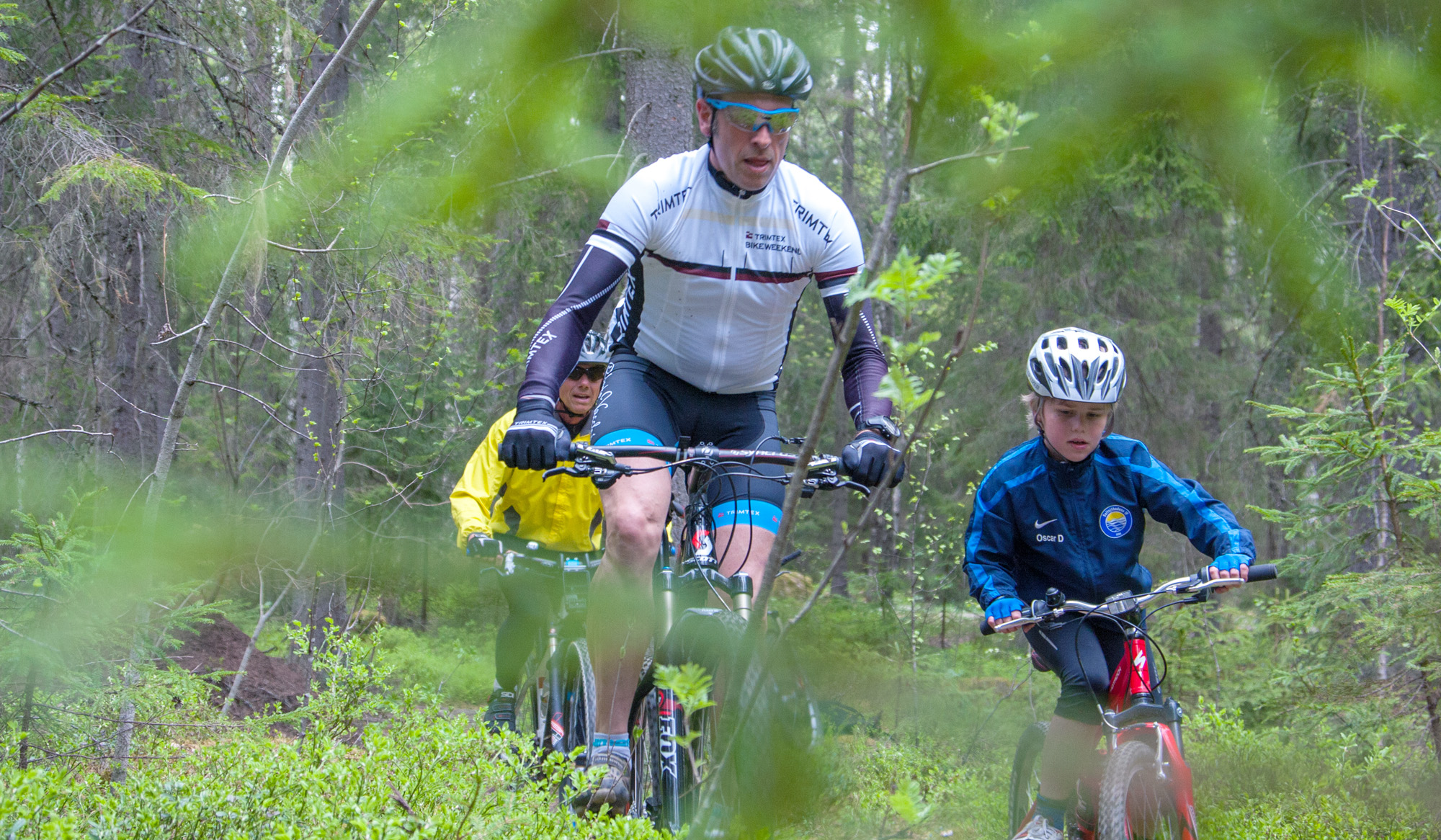 En man och två barn cyklar mountainbike i skogen