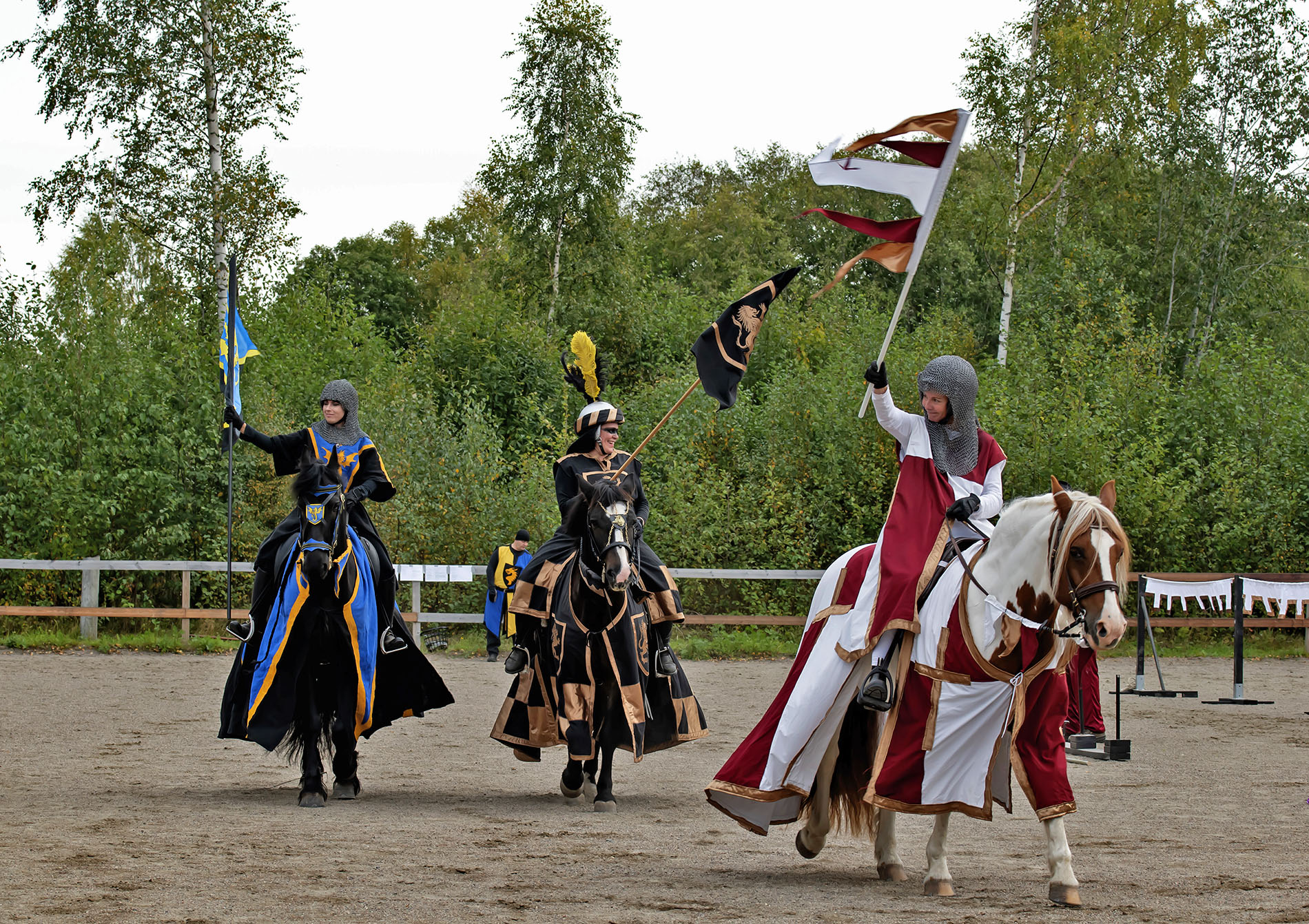 Tre personer utklädda till riddare rider på hästar i ett tornerspel. 