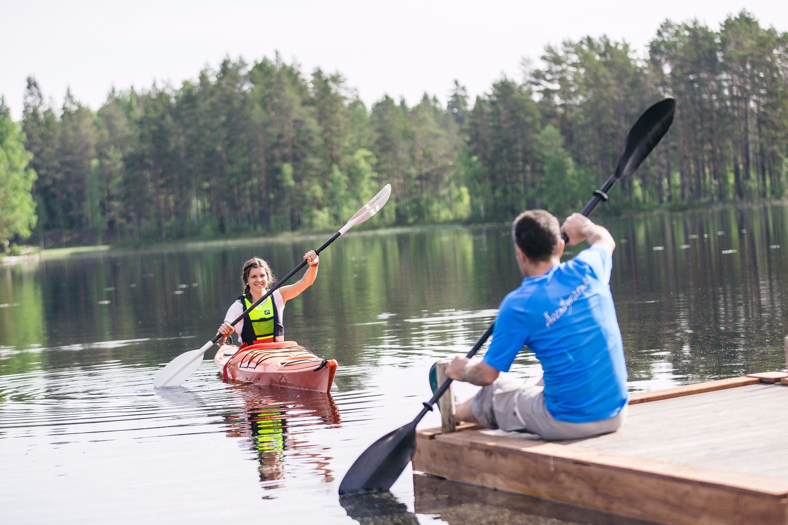 En flicka i kanot övar på paddlingsrörelser. En man instruerar från bryggan. 