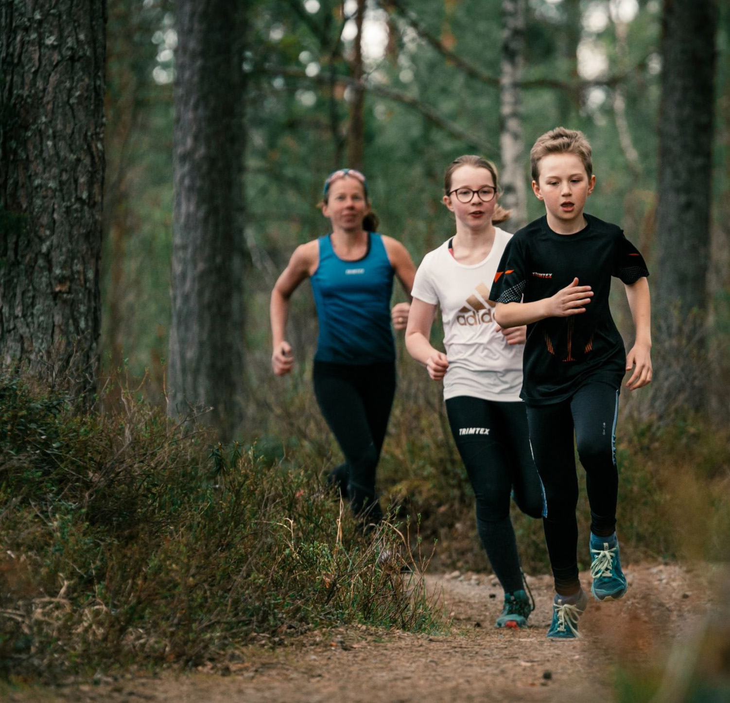 Tre unga löpare på en stig i skogen
